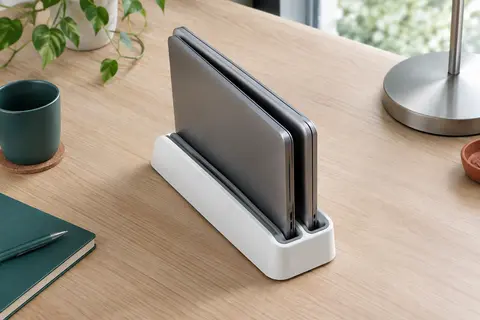 Socle vertical blanc à deux rainures avec deux ordinateurs portables fermés rangés debout côte à côte, sur un bureau en bois clair