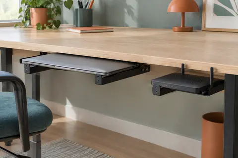 Trois pattes en fer noir perforé vissées sous un bureau en bois clair, deux portant un ordinateur portable fermé et la troisième un routeur plat